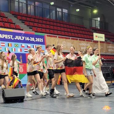 Gruppe von Jugendlichen in bunten T-Shirts, die eine Deutschlandflagge halten und auf einer Bühne stehen.