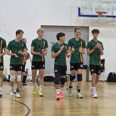 Gruppe von zehn jungen Menschen in grünen Trikots marschiert auf einem Sportplatz, klatscht in die Hände.