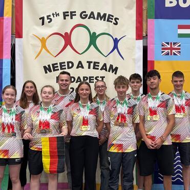 Gruppe von zehn Personen in sportlichen Shirts mit Medaillen, posierend vor einem farbigen Hintergrund der 75. FF Games.