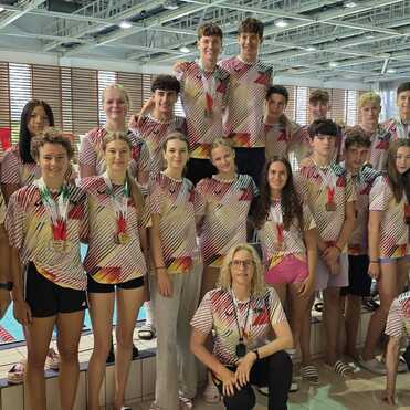 Gruppe von Schwimmern in bunten Trikots steht am Beckenrand eines Schwimmbads und lächelt in die Kamera.