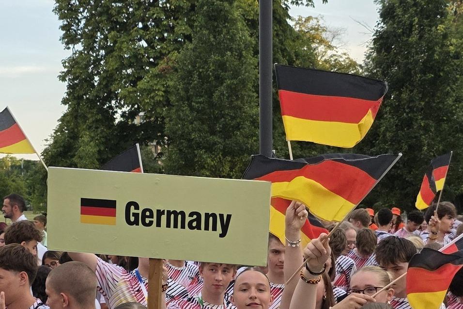 Gruppe junger Menschen mit Deutschlandfahnen, eine Person h&auml;lt ein Schild mit &bdquo;Germany&ldquo; und alle tragen einheitliche T-Shirts.