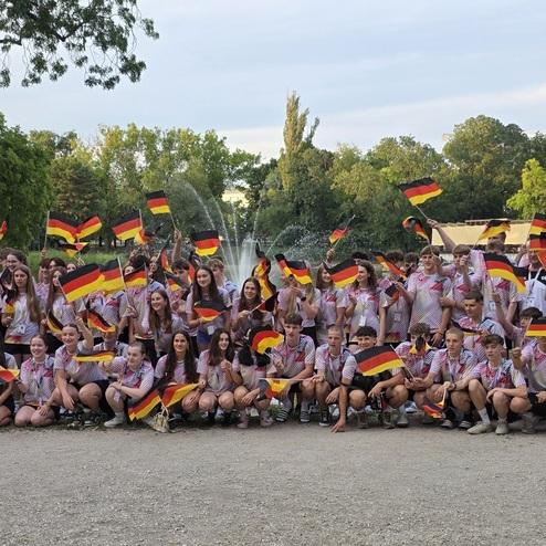 Gruppenfoto von circa 70 Personen im Park, die Deutschlandflaggen schwenken und einheitliche T-Shirts tragen.