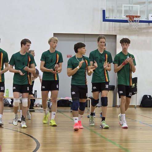 Gruppe von zehn jungen Menschen in gr&uuml;nen Trikots marschiert auf einem Sportplatz, klatscht in die H&auml;nde.