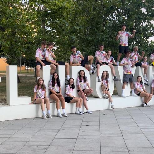 Gruppe junger Menschen sitzt und steht um ein gro&szlig;es, dekoratives #LLN030-Schild auf einem Stadtplatz.
