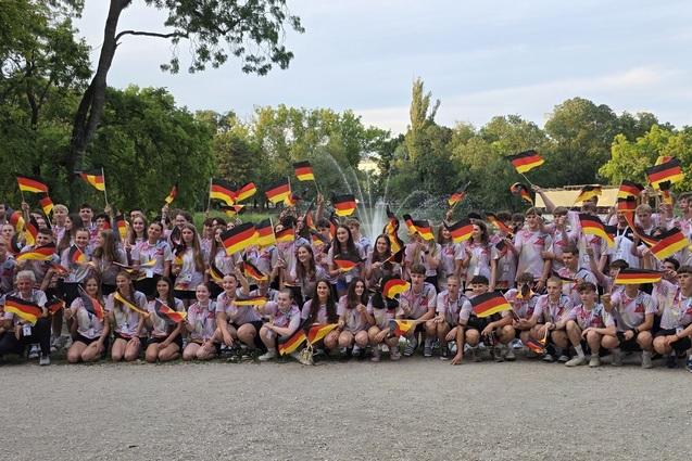Gruppenfoto von circa 70 Personen im Park, die Deutschlandflaggen schwenken und einheitliche T-Shirts tragen.