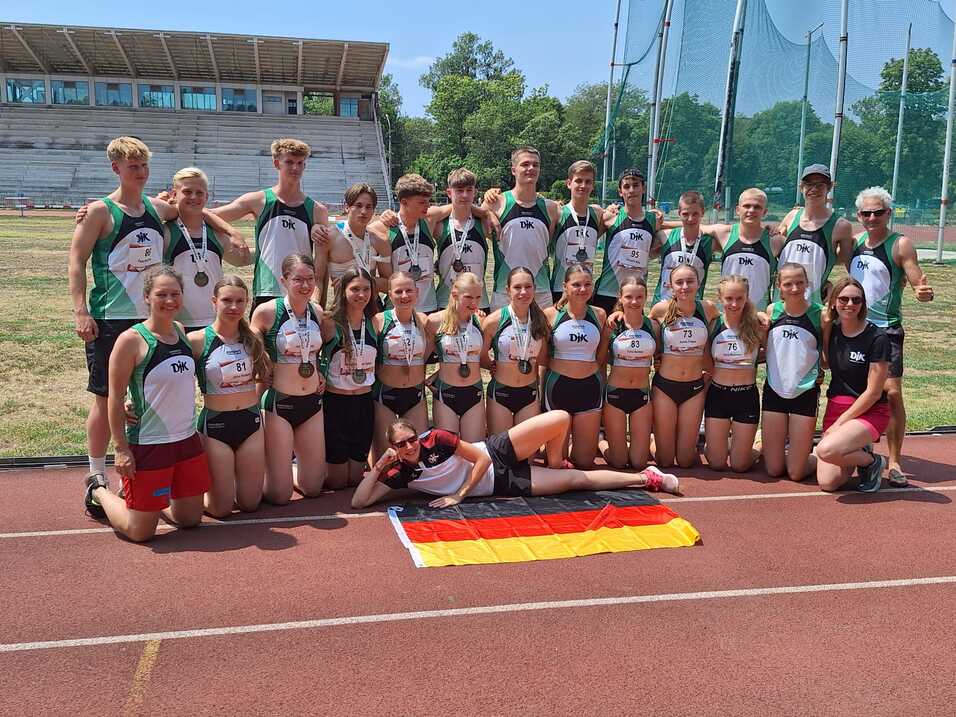 Gruppe junger Athleten in Sportbekleidung posiert auf einer Laufbahn mit einer deutschen Flagge.