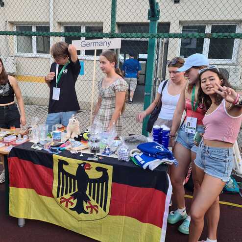 Gruppierung junger Menschen am Tisch mit deutscher Flagge, der diverse Gegenst&auml;nde und Souvenirs pr&auml;sentiert.