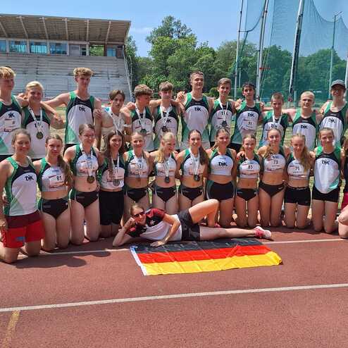 Gruppe junger Athleten in Sportbekleidung posiert auf einer Laufbahn mit einer deutschen Flagge.