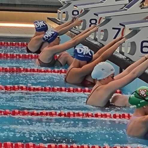 Vier Schwimmerinnen bereiten sich an Startbl&ouml;cken im Wettkampfbecken auf den Start ihres Rennens vor.