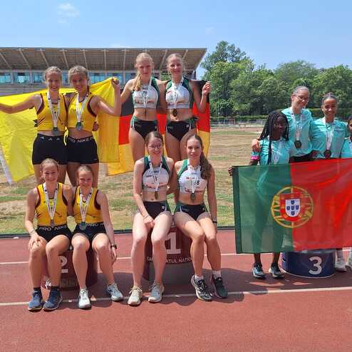 Zehn junge Athletinnen halten Medaillen und Fahnen von Deutschland und Portugal auf einem Sportplatz.