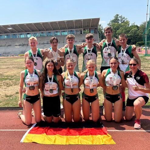 Gruppensportler stehen auf einer Laufbahn, pr&auml;sentieren Medaillen, mit einer deutschen Flagge im Vordergrund.