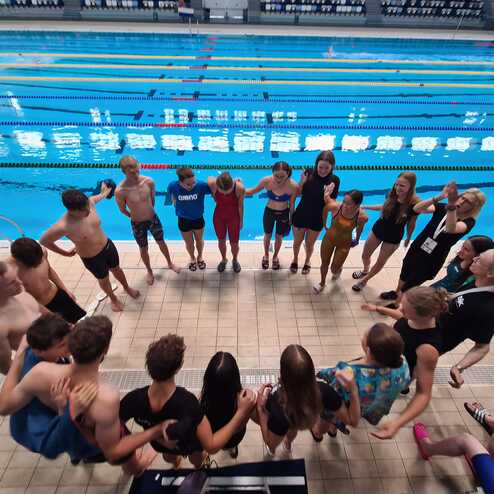 Gruppe von Schwimmern steht in einem Kreis am Rand eines Schwimmbeckens mit Wasserbahnen.