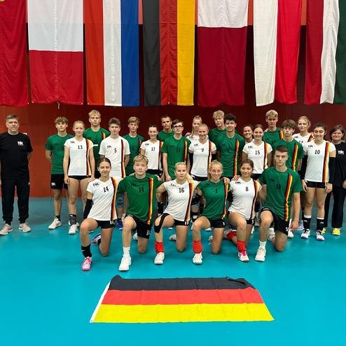 Gruppenbild von einem Volleyballteam mit Spielern in gr&uuml;nen und wei&szlig;en Trikots, vor bunten Fahnen und der deutschen Flagge.