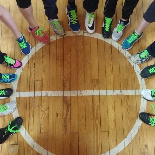 Zehn Sportler stehen in einem Kreis, ihre F&uuml;&szlig;e mit bunten Schuhen und gr&uuml;nen Schn&uuml;rsenkeln auf einem Basketballfeld.
