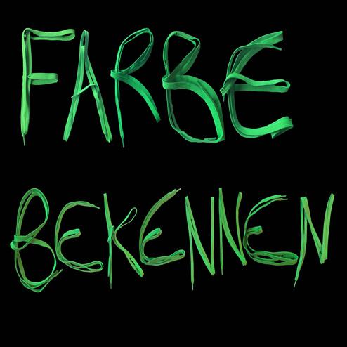 Gr&uuml;ne, zusammenh&auml;ngende Buchstaben formen die Worte &bdquo;FARBE BEKENNEN&ldquo; vor schwarzem Hintergrund.
