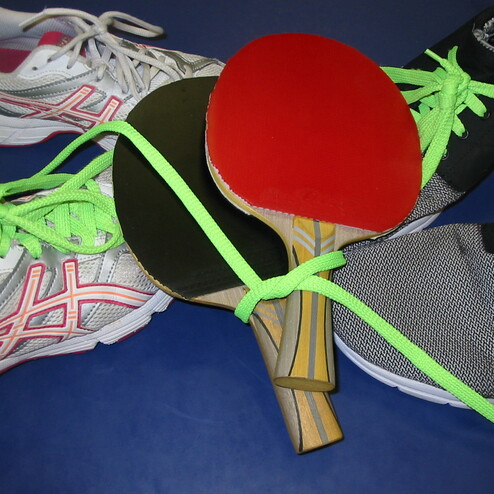 Verschiedene Tischtennisschl&auml;ger und Sneakers mit gr&uuml;nen Schn&uuml;rsenkeln auf blauem Untergrund.