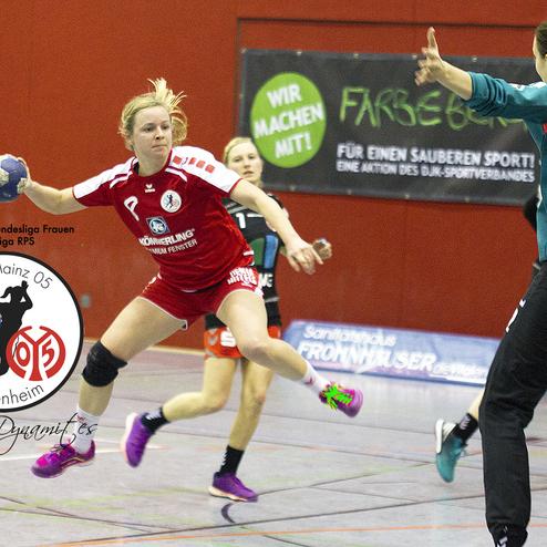 Handballspielerin in rotem Trikot springt zum Wurf, im Hintergrund Spielerin in gr&uuml;nem Trikot und Hallenwand.