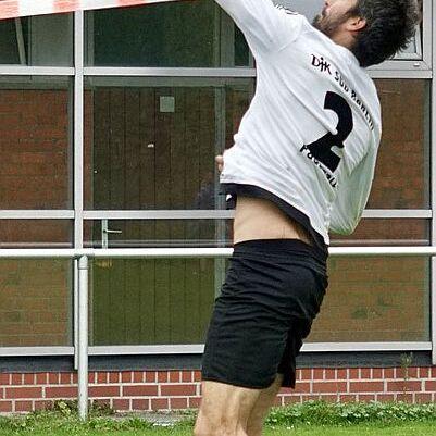 Spieler in weißem Trikot springt, um einen Ball über ein Netz auf einem Sportplatz zurückzuspielen.