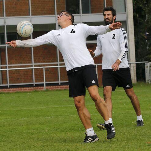 Zwei Männer in Sportkleidung trainieren im Freien, während einer einen Ball zu fangen versucht.