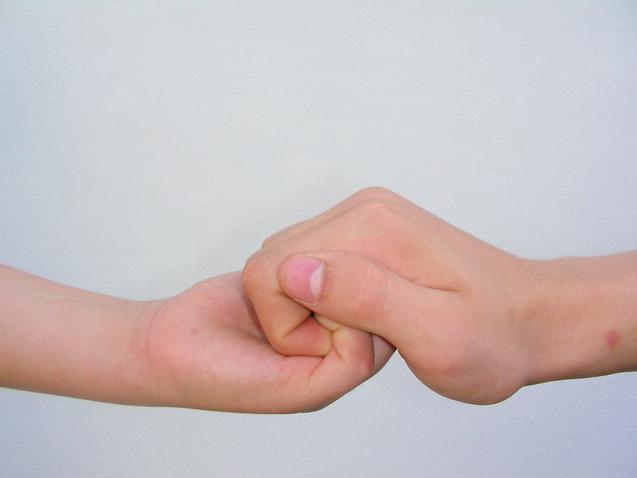 Zwei H&auml;nde, eine kindliche und eine erwachsene, halten sich in einem festen H&auml;ndedruck vor einem neutralen Hintergrund.