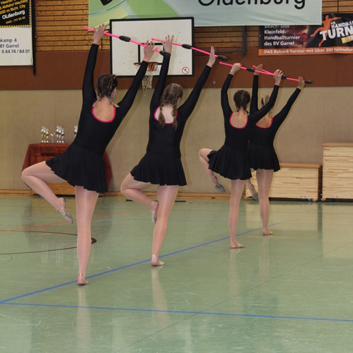 F&uuml;nf T&auml;nzerinnen in schwarzen Kost&uuml;men f&uuml;hren eine Choreografie mit St&auml;ben in einer Sporthalle auf.