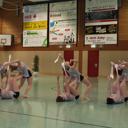 Gruppe von T&auml;nzerinnen f&uuml;hrt eine Choreografie mit wei&szlig;en B&auml;ndern in einer Sporthalle auf.