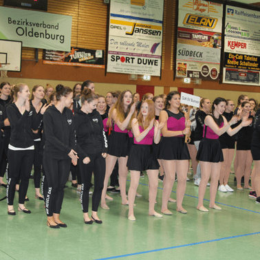 Gruppe junger T&auml;nzerinnen in Sportkleidung klatscht und wartet auf ihren Auftritt in einer Sporthalle.