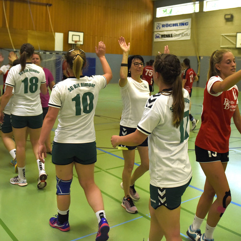 Mannschaftsmitglieder beider Handballteams begr&uuml;&szlig;en sich mit erhobenen H&auml;nden in einer Halle.