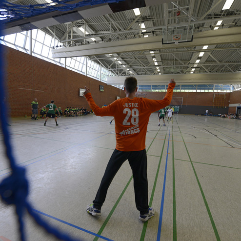 Torwart in orange mit der Nummer 29 steht in der Halle und signalisiert w&auml;hrend eines Handballspiels.