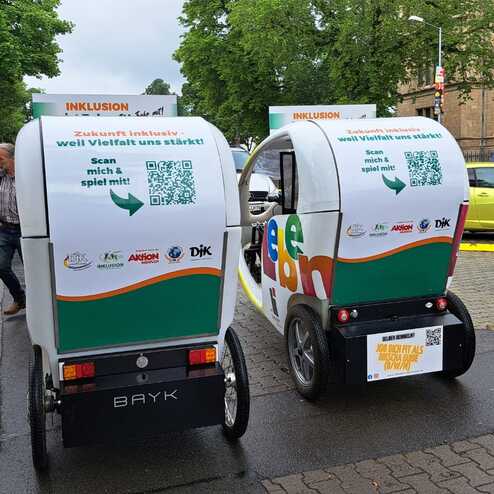 Zwei farbige Rickshaws stehen auf einer Stra&szlig;e, jeweils mit QR-Codes und Werbebotschaften auf den R&uuml;ckseiten.