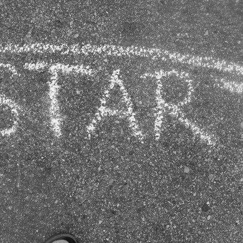 Wei&szlig;es &bdquo;START&ldquo;-Schild aus Kreide auf asphaltierter Fl&auml;che, leicht von oben betrachtet.