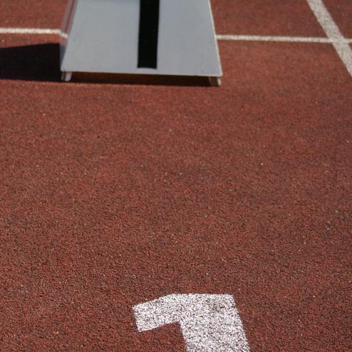 Block mit der Startnummer 1 auf einem roten Laufbahn-Untergrund mit wei&szlig;er Markierung der gleichen Zahl.