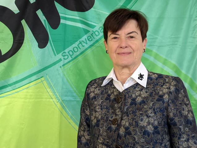 Frau mit k&uuml;rzeren Haaren, in einer eleganten Jacke, steht vor einem gr&uuml;nen Banner mit dem Schriftzug &bdquo;DiK Sportverband&ldquo;.