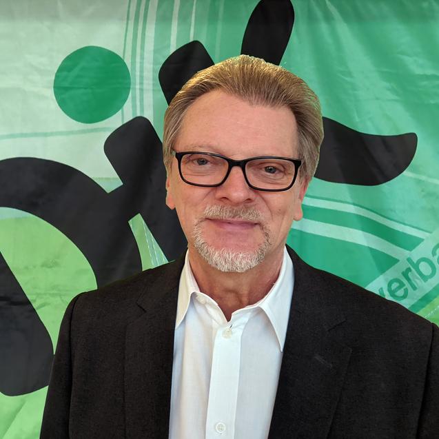 Portr&auml;t eines Mannes mit Brille vor einem gr&uuml;nen Hintergrund mit dem Schriftzug &bdquo;Dix&ldquo; und grafischen Elementen.