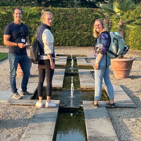 Drei Personen stehen auf einem Gartenweg mit Wasserfont&auml;nen, umgeben von Pflanzen und einem gepflegten Landschaftsgarten.