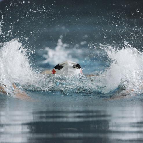 Schwimmer taucht mit einem Kopf &uuml;ber Wasser in ein Becken, Wasser spritzt um ihn herum.