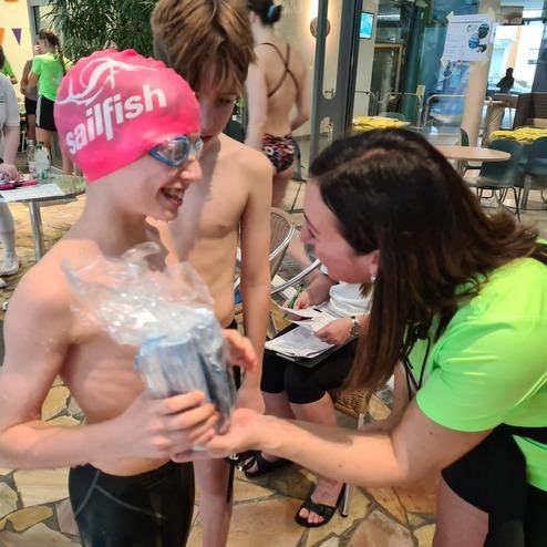Junge Schwimmer in Badekappe und Brille erh&auml;lt eine Auszeichnung von einer Trainerin in einem Schwimmbad.