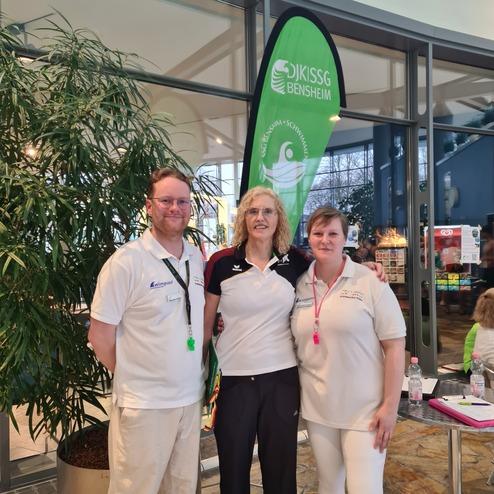 Drei Personen in Sportkleidung stehen neben einer gr&uuml;nen Fahne mit dem Logo des Vereins KSSG Bensheim.