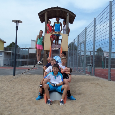 Gruppe von Kindern sitzt auf einer Rutsche und Sandkasten, w&auml;hrend einige auf einem Spielturm stehen.