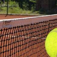 Nahaufnahme eines gelben Tennisballs, der an einem Tennisnetz auf einem roten Sandplatz schwebt.
