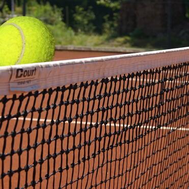 Tennisball schwebt &uuml;ber dem Netz auf einem roten Tennisplatz im Freien.