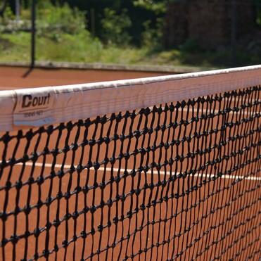 Nahaufnahme eines Tennisnetzes auf einem Sandplatz, mit Sonnenlicht und gr&uuml;nem Hintergrund.