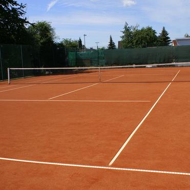 Leere Tennisplatz mit roter Sandoberfl&auml;che und wei&szlig;en Linien, umgeben von gr&uuml;nen B&auml;umen und einem Zaun.