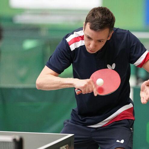 Tischtennisspieler in Aktion, schl&auml;gt einen Ball mit einem Schl&auml;ger auf einem Tischtennistisch.