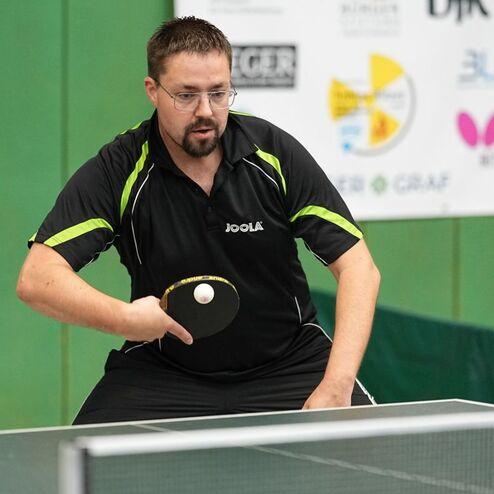 Tischtennisspieler in Aktion, bereit, einen Ball mit Schl&auml;ger auf einer gr&uuml;nen Tischtennisplatte zu schlagen.