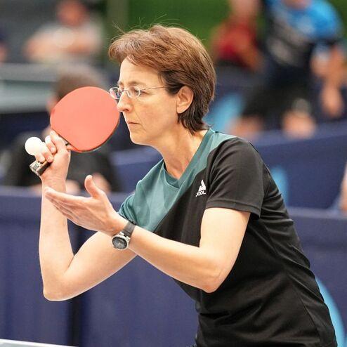 Eine Spielerin bereitet sich auf den Schlag mit einem roten Tischtennisschl&auml;ger an einem Tischtennistisch vor.