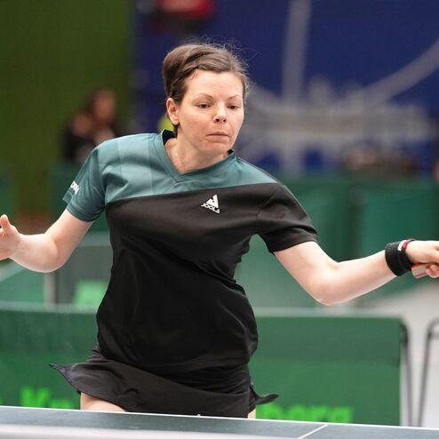 Spielerin in Aktion, die einen Tischtennisball mit einem Schl&auml;ger auf einem Tischschl&auml;gerfeld schl&auml;gt.