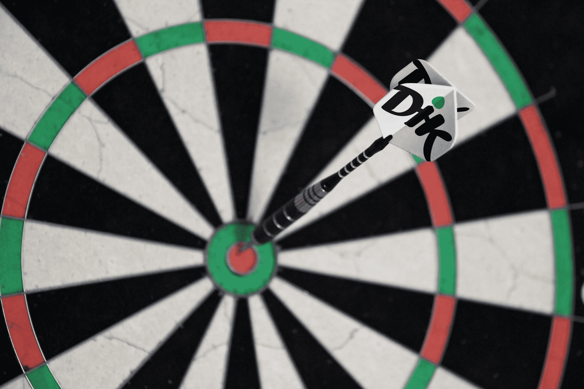 Pfeil steckt ins Bullseye einer traditionellen Dartscheibe mit schwarzem, gr&uuml;nem und rotem Muster.
