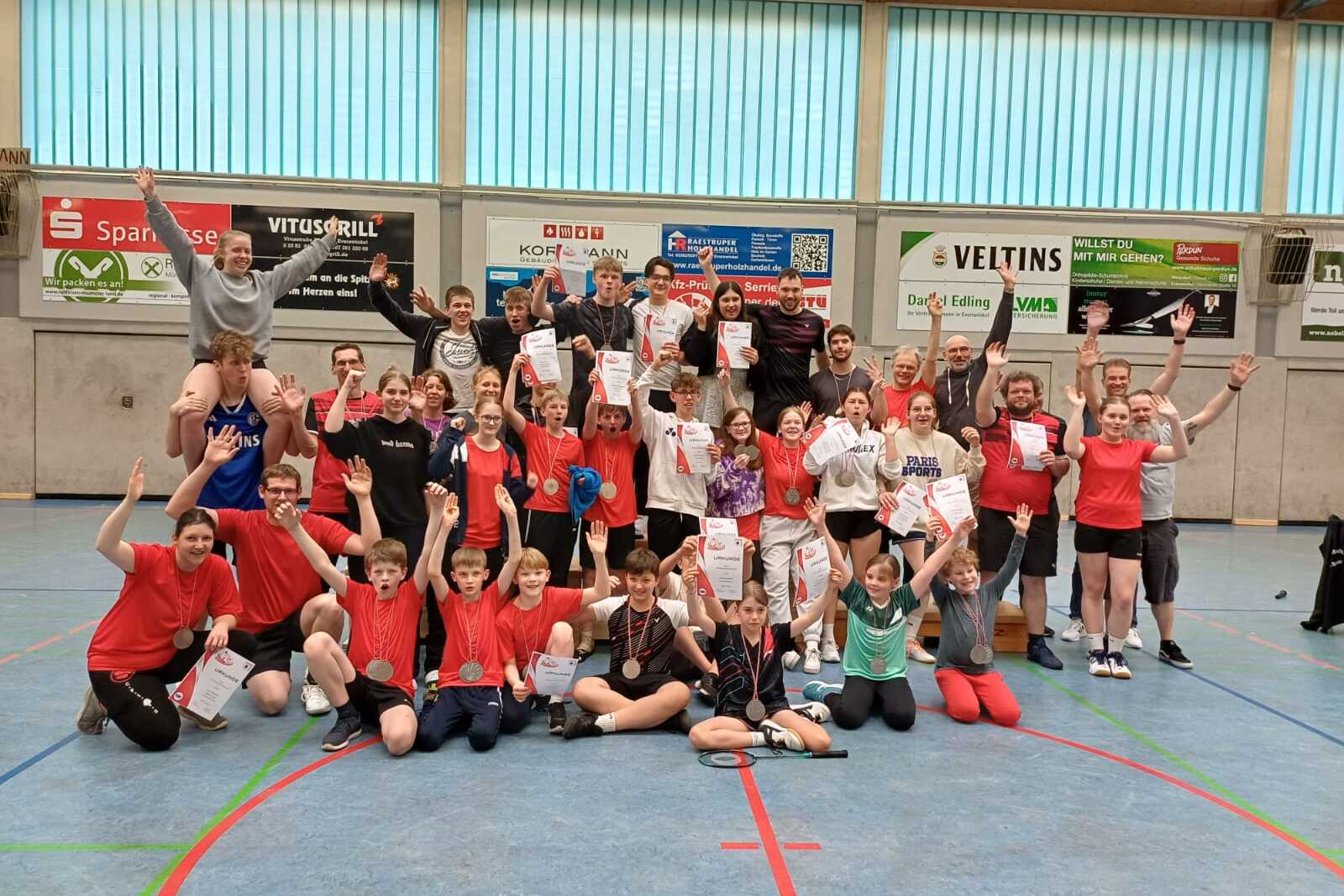 Gruppenfoto von 40 Personen in Sportkleidung, die jubelnd mit Urkunden in einer Sporthalle stehen.