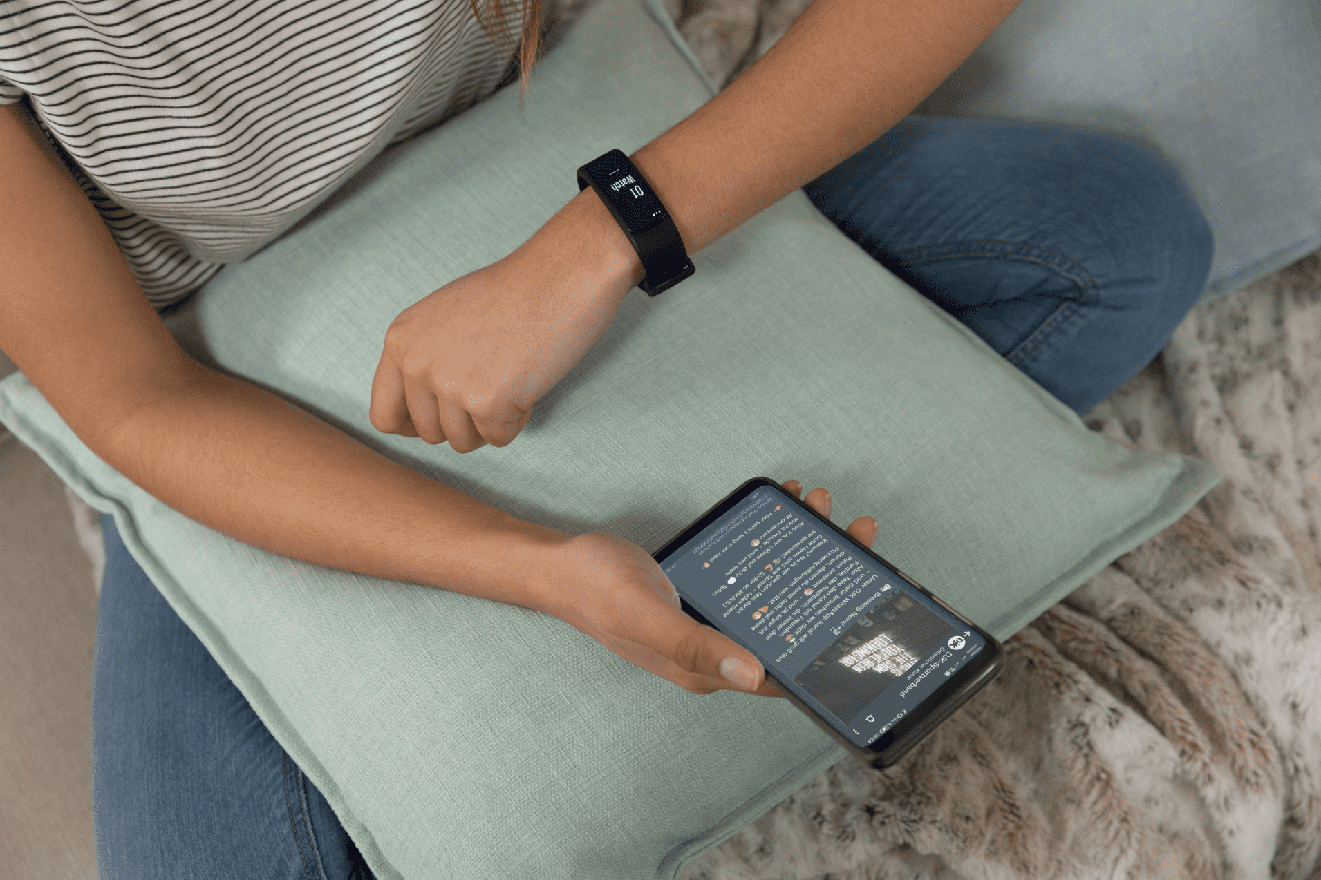 Junge Frau mit Fitness-Armband schaut auf ihr Smartphone, w&auml;hrend sie auf einem Kissen sitzt.